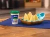 Fotografia de uma bancada de madeira com um pano azul escuro. Sobre ele tem um recipiente quadrado de madeira com um pano azul e branco forrando as quatro coxinhas saudáveis que estão dentro. Ao lado do recipiente tem um pote de requeijão light.