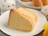 Fotografia de fatias de um bolo de queijo leve e fofinho em um prato elegante. O cenário festivo inclui ovos decorados e uma pétala de flor amarela, transmitindo uma atmosfera de celebração e aconchego.
