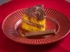Fotografia de um pedaço de bolo de cenoura com recheio e cobertura de ganache de kiktat em um prato vermelho com um kitkat sobre um pano vermelho.