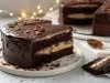 Em cima de uma mesa, prato redondo com fatia de bolo de chocolate fofinho, recheado com creme branco e com cobertura de chocolate.