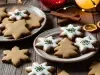 Em cima de uma mesa, prato redondo com biscoitos em forma e estrelas e árvore de Natal, decorados com glacê branco e confeitos de bolinhas coloridas.
