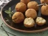 Imagem de um prato rústico preto com diversos bolinhos arancini e um bolinho ao meio mais a frente.