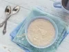 Imagem vista de cima de um bowl azul claro sobre paninhos azuis com mingau de aveia. Ao lado, duas colheres e ao fundo uma xícara azul com café.