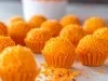 Fotografia mostra brigadeiros laranjas em forminhas laranja sobre uma mesa de madeira.