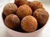 Em cima de uma mesa, tigela com bolinhos redondos, polvilhado com açúcar e canela.