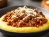Fotografia mostra um angu cremoso, coberta com carne moída bem temperada e queijo mussarela por cima.