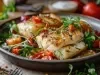Em cima de uma mesa, frigideira com postas de bacalhau com tomate cereja e pimentões, decorado com folhas verdes.