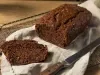 Em cima de uma mesa, grade com bolo de chocolate cortado em um fatia.