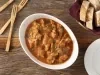 Imagem vista de cima de uma travessa branca com a receita de moela de frango e uma cesta de pães ao lado.