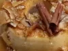 Fotografia de um pudim de cocada cremosa decorado com a calda com coco, lascas de coco e paus de canela.