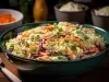 Em cima de uma mesa,  tigela com salada de maionese cremosa e colorida com cenouras raladas e repolho roxo ralado, decoradas com folhas de cheiro-verde.