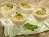 Imagem de quatro taças de mousse de maracujá decoradas com sementes de maracujá e folhas de hortelã.