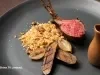 Costeleta de cordeiro ao ponto com farofa de castanhas, legumes grelhados e molho servido em pequeno recipiente.