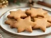 Em cima de uma mesa com enfeites de Natal, prato redondo com biscoitos em formato de estrelas.