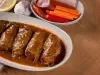 Em cima de uma mesa, refratário com bifes suculentos enrolados com molho de tomate, decorado com ervas.