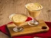 Imagem de duas taças de vidro com a receitas de mousse de maracujá sobre uma tábua de madeira e um pano vermelho.