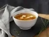 Imagem de uma tigela branca com sopa de missoshiro em cima de uma tábua preta. Ao lado, pedaços de cebolinha.
