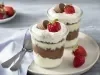 Imagem de dois copos com a receita mostrando as camadas de recheio decoradas com morango e um bombom.