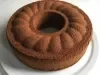 Em cima de uma mesa, prato branco redondo com bolo com furo no meio de chocolate fofinho.