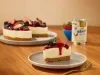 Fotografia mostra uma fatia de cheesecake de frutas vermelha. Ao fundo, o restante da chessecake e a lata de leite moça.