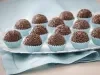 Foto de um prato branco que está em cima de um pano azul com vários brigadeiros dentro de forminhas azuis