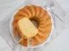 Fotografia de um bolo bundt recém-assado em um prato branco, com crosta dourada e interior fofinho, pronto para ser servido, acompanhado de dois garfos prateados em um ambiente acolhedor.