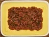 Foto bem aproximada de uma travessa branca. Dentro dela está a receita de polenta em tom amarelo claro e, ao centro, a carne moída com molho