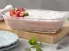 Imagem de uma travessa transparente com a receita de pavê mostrando as camadas, decorado com coco ralado e morangos.