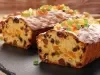 Fotografia de um bolo de frutas natalino, com uma camada generosa de frutas cristalizadas coloridas no topo. O bolo, cortado, revela um interior rico e vibrante.