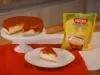 imagem mostra uma cheesecake cremosa de milho com cobertura de goiabada em uma forma redonda.
