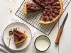 Fotografia vista de cima em tons claros de uma fatia de torta de nozes e doce de leite em um prato raso médio branco. Ao lado tem o restante da torta sobre uma grade preta.