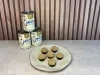 Prato com docinhos cobertos com farofa crocante e latas de Leite Moça empilhadas ao fundo.