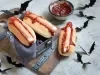 Cachorro-quente com salsichas em formato de dedo, pão macio e dourado, corte superficial na ponta simulando unha, com ketchup vermelho escorrendo.