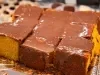 Bolo de cenoura cortado em pedaços quadrados, coberto com uma camada generosa de calda de chocolate brilhante. Os pedaços estão organizados sobre uma bandeja metálica.