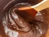 Fotografia da mistura do brigadeiro cremoso de chocolate em uma panela de alumínio, com uma colher de pau mexendo o brigadeiro.