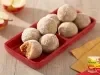 Doces de maçã em formato de bolinhas, cobertos com açúcar, dispostos em travessa vermelha, com maçãs ao fundo.