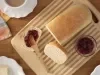 Imagem vista de cima de um pão caseiro cortado e uma fatia com geleia. Ao lado, um potinho de geleia de frutas vermelhas.