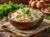 Em cima de uma mesa, travessa com salada de maionese com cenoura, batata, presunto e ervilha. Decorado com folhas de salsa.