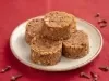 Cocadas cremosas em formato cilíndrico, com textura de coco e café, dispostas em prato sobre mesa vermelha.