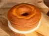 Bolo dourado com furo central, de textura levemente crocante por fora e macia por dentro. Está sobre um prato branco e uma tábua de madeira, iluminado pela luz natural.