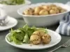Imagem de um prato com batata calabresa e uma salada verde ao lado. Ao fundo, uma travessa com batatas.