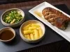 Pernil suíno assado com mandioca dourada, salada de folhas com laranja e molho servido à parte, apresentado em travessas.