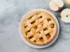 Imagem vista de cima de um prato branco com uma torta de maçã trançada com dois pedaços de maçãs cortadas ao meio.