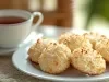 Em cima de uma mesa, prato redondo branco com biscoitos dourado com coco.