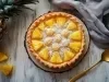 Fotograifa vista de cima de uma torta de abacaxi com coco por cima em um recipiente claro de madeira sobre uma mesa de madeira de tom claro.