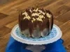 Foto aproximada de um bolo de chocolate com decoração de lascas marmorizadas, sobre um prato branco e azul em uma bancada de madeira