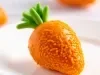 Fotografia mostra brigadeiro em formato de cenoura sobre um prato raso branco.