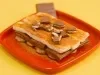 Sobremesa em prato vermelho com banana, creme claro, chocolate recheado e canela por cima.