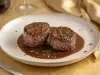 Dois medalhões de filé mignon, servidos com molho reduzido escuro e brilhante, apresentados em prato branco sofisticado
