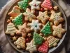 Em cima de uma mesa, prato com biscoitos em formato de estrelas, sinos e árvores de Natal, decorados com glacê colorido e confeitos coloridos de bolinhas verde e vermelho.